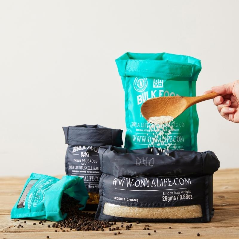 Small, Medium, Large, Aqua and Charcoal colored Onya bulk food bags holding food items that are being used to fill up pantry containers. Available at Green Distributors.