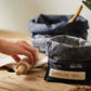 Onya Charcoal colored bulk food bags holding flour as a baker rolls out dough on a wooden surface. Available at Green Distributors.