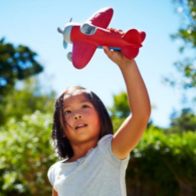 A child is pretending a Green Toys Airplane with red wings is flying in the sky. Available at Green Distributors.