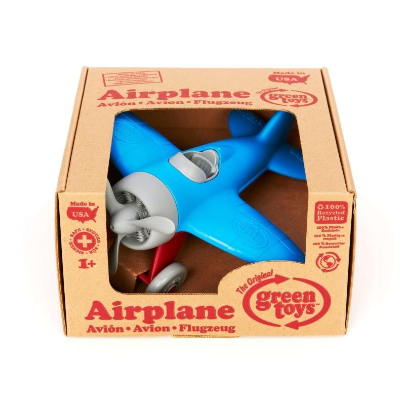 Green Toys Airplane with blue wings, red landing gear, gray propeller, cockpit, and wheels. The airplane is shown inside the cardboard box packaging. Available at Green Distributors.