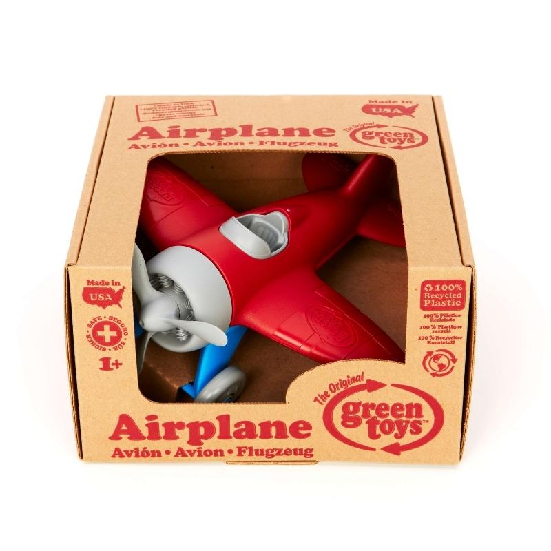Green Toys Airplane with red wings, blue landing gear, gray propeller, cockpit, and wheels. The airplane is shown inside the cardboard box packaging. Available at Green Distributors.