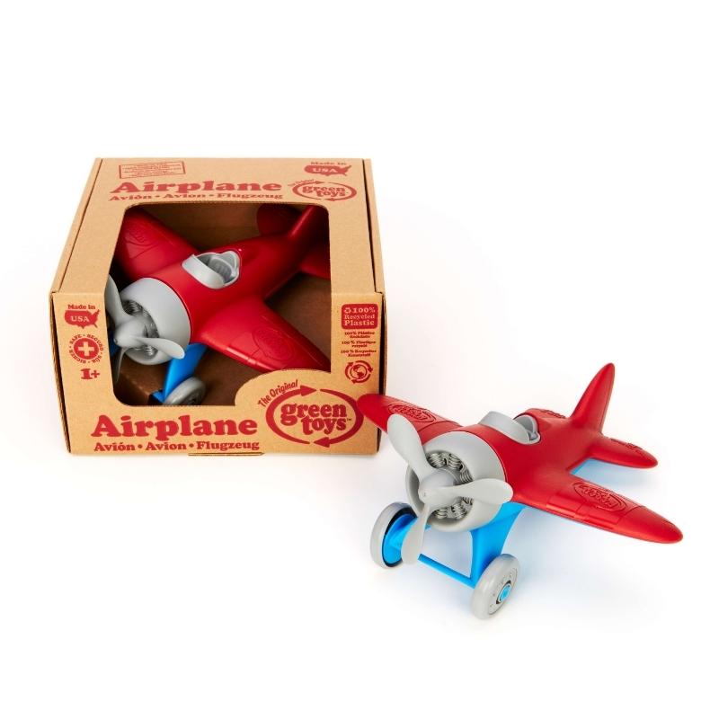 Green Toys Airplane with red wings, blue landing gear, gray propeller, cockpit, and wheels. The airplane is shown both inside and outside of cardboard box packaging. Available at Green Distributors.