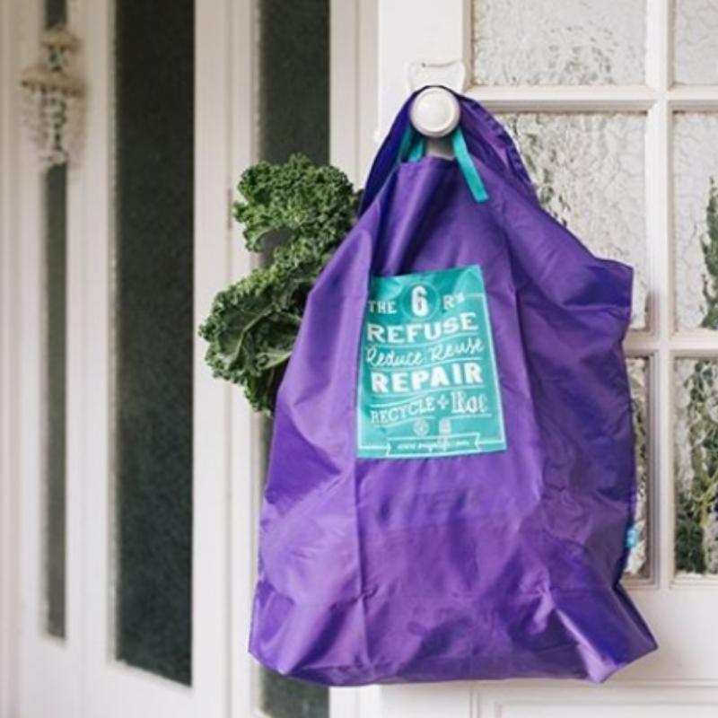 Onya large, purple, reusable shopping bag with the 6 R's:  Refuse, Reduce, Reuse, Repair, Recycle & Rot. The bag is holding items from the grocery store and hangs from a door knob. Available at Green Distributors.