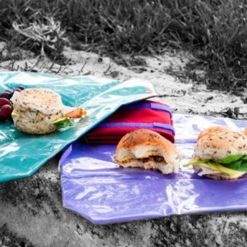 An impromptu picnic of sandwiches and grapes is set up using Onya reusable lunch wraps as placemats alongside a hiking trail. Available from Green Distributors.